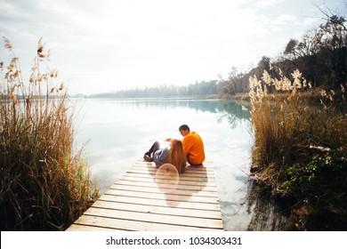 Young hipster couple of millennials, love birds sit on pier in park overlook big lake or river during autumn season. Hug and cuddle cosy and romantic, talk about future plans and travel destination - Powered by Shutterstock