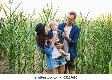 Young Hipster Family With Cute Baby In Hands In The Cornfield Smiling And Playing
