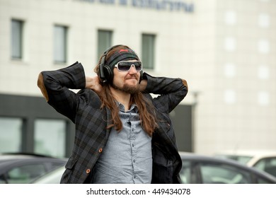 Young hipster fashion guy with beard. The man with the headphones on his head listening to music and walking in the city. - Shutterstock ID 449434078