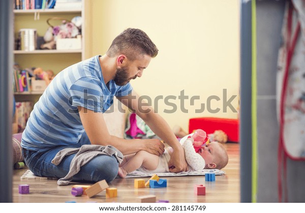 Young hipster father changing nappy to his\
little baby daughter