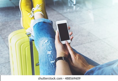 Young Hipster Girl At Airport In Yellow Boot On Suitcase Waiting Air Flight, Female Hands Holding Smart Phone In Terminal Departure Lounge Gate, Traveler Trip Concept, Mockup Of Blank Screen Sellphone