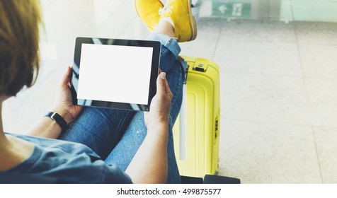 Young hipster girl at airport in yellow boot on suitcase waiting air flight, female hands holding computer in terminal departure lounge gate, traveler trip concept, mock up of blank screen tablet - Powered by Shutterstock