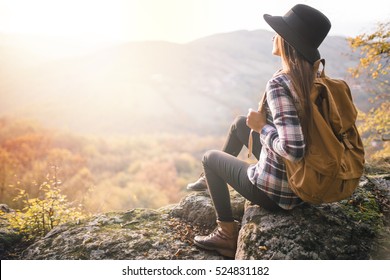 Young Hipster Girl Enjoy Sunset On Viewpoint. Travel Woman With Backpack And Hat