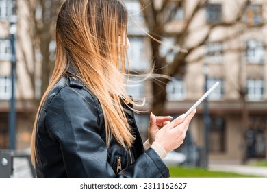 Young hipster girl holding pc tablet in the city.Traveler woman using tablet.reading guide book map on tablet computer pc,using mobile internet.Female writes text message or content. - Shutterstock ID 2311162627