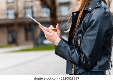 Young hipster girl holding pc tablet in the city.Traveler woman using tablet.reading guide book map on tablet computer pc,using mobile internet.Female writes text message or content. - Shutterstock ID 2320029839