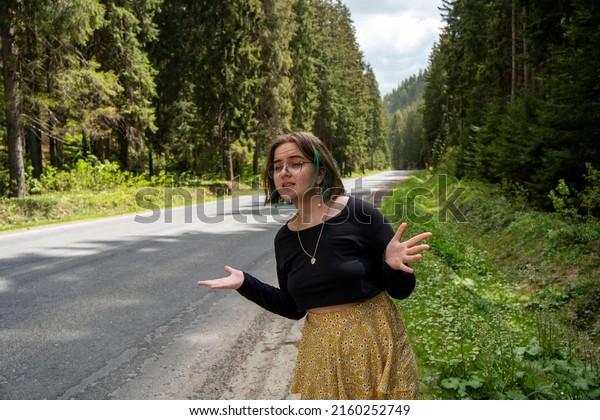Young hipster girl lost and looking for\
a car on the country road. Travel woman hitchhiking on road trip\
hitching a ride from car in amazing landscape\
nature.