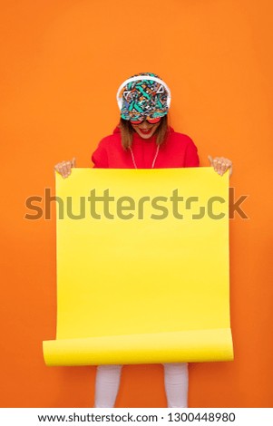 young and hipster girl presenting an yellow empty roll of papper, space for text, on orange background