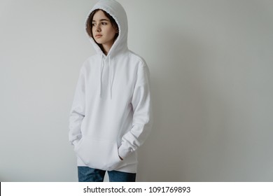 Young hipster girl wearing white oversize women hoodie with blank space for your logo or design, mock-up of white sporty cotton sweatshirt, white wall in the background