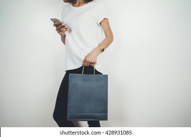 Young Hipster Girl Wearing White T-shirt And Holding Blank Blue Shopping Bag, Mock-up Of Blue Paper Package, White Background