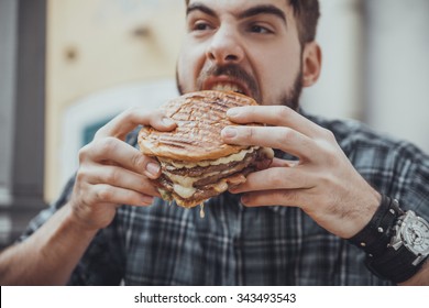 Young Hipster Male In Pub Eating Delicious Burger