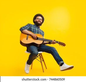 Young hipster man in casual clothing sitting on chair playing guitar smiling at camera on orange background.  - Powered by Shutterstock