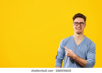 Young Hipster Man In Glasses And Blue Jumper Pointing Happily Away On Orange Yellow Background