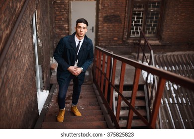 Young hipster man on stairs. A man wearing in a blue jacket , a white shirt, blue jeans and yellow boots - Shutterstock ID 375825823