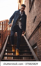 Young hipster man on stairs. A man wearing in a blue jacket , a white shirt, blue jeans and yellow boots - Shutterstock ID 375825829