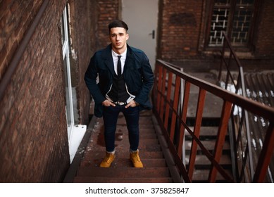 Young hipster man on stairs. A man wearing in a blue jacket , a white shirt, blue jeans and yellow boots - Shutterstock ID 375825847
