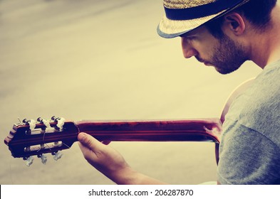 Young Hipster Man Plays The Guitar On The Street. Musician With Hat Plays The Music. Retro Filter Style.