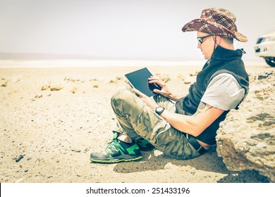 Young Hipster Man Sitting In Desert Road - Concept Of Modern Technologies With A Alternative Travel Lifestyle - Overexposed Vintage Desaturated Filtered Look With Focus On The Hand Using The Laptop 