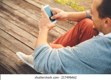 Young  Hipster Man Using Smart Phone Sitting On Wooden Boards