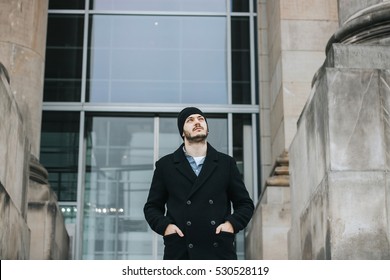 Young hipster man walking down the stairs with hands in pockets and looking up toward the sky, in front of modern building entrance - Powered by Shutterstock