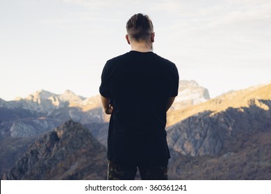 young hipster man wearing a black blank t-shirt on the mountain background. Back view