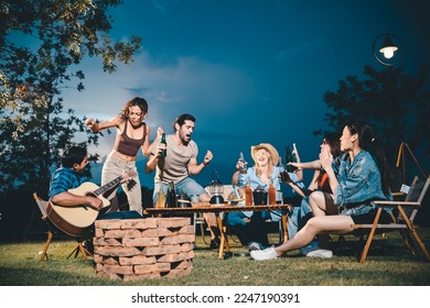 Young hipster people having fun to music dining and drinking together in campsite - Travel vacation lifestyle and youth culture concept, Happy friends group toasting beers at barbecue camping party - Powered by Shutterstock