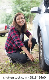 Young hipster woman checking out a flat tyre on her car try to fix.