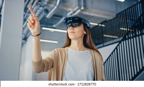 Young Hipster Woman in Holographic Augmented Reality Glasses Standing in Empty Office and Map it. Sunlight Shines Through Big Windows.