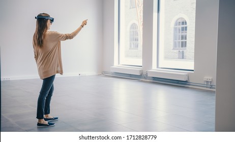 Young Hipster Woman in Holographic Augmented Reality Glasses Standing in Empty Office and Map it. Sunlight Shines Through Big Windows. - Powered by Shutterstock