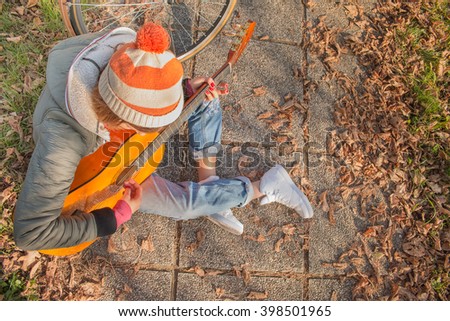 young hipster woman play guitar sitting on the ground wearing fashionable jeans - view from top - motion blur on strumming fingers, with custom color tones 