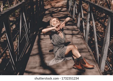 Young Hipster Woman Travels In Colorado Forest. Wooden Bridge In The Forest. Long Dress, Chelsea Boots. Blonde Millennial Lady. Freedom. Escape Home. Local Traveling. Exploring Places. Travel Locally