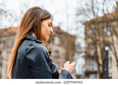 Young hipster woman using a smartphone in the city.female blogger typing text message on her cellphone.Side view. - Shutterstock ID 2307949343