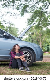 Young hipster woman waiting for roadside assistance after her car breaks down at the side of the road sitting against her car.