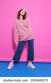 Young Hipster Woman Wearing Pink Sweatshirt, Hat, Jeans And Sneakers. Fashion Studio Shot