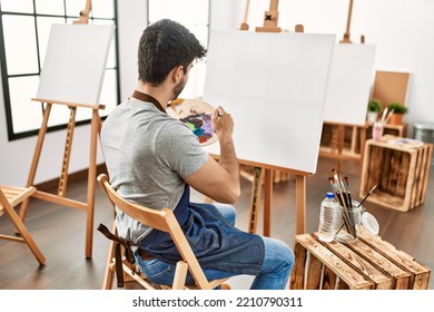 Young hispanic artist man onback view painting at art studio 