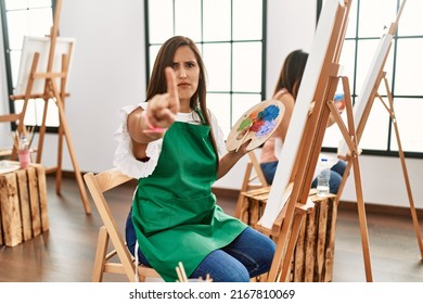 Young Hispanic Artist Women Painting On Canvas At Art Studio Pointing With Finger Up And Angry Expression, Showing No Gesture 