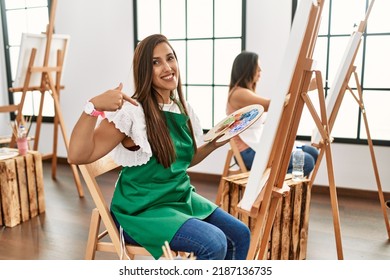 Young hispanic artist women painting on canvas at art studio looking away to side with smile on face, natural expression. laughing confident.  - Shutterstock ID 2187136735