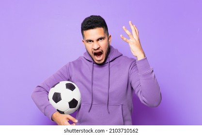 young hispanic athlete man angry expression and holding a soccer ball