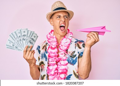 Young Hispanic Boy Wearing Summer Style Holding Dollars And Paper Airplane Angry And Mad Screaming Frustrated And Furious, Shouting With Anger. Rage And Aggressive Concept. 