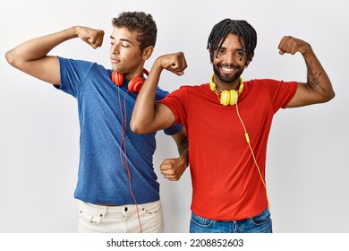 Young Hispanic Brothers Standing Over Isolated Background Wearing Headphones Showing Arms Muscles Smiling Proud. Fitness Concept. 