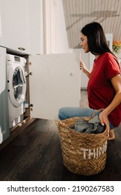 Young Hispanic Brunette Woman Putting Clothes At Washing Machine While Doing Laundry At Home