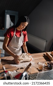 Young Hispanic Brunette Woman Wearing Apron Cooking And Kneading Dough In Kitchen At Home