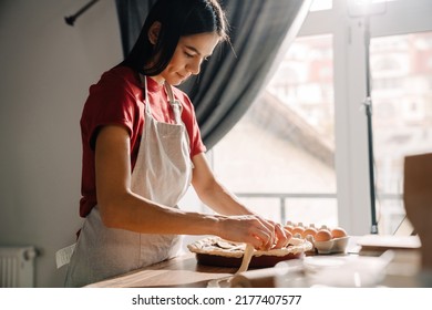 Young Hispanic Brunette Woman Wearing Apron Cooking And Making Pie In Kitchen At Home