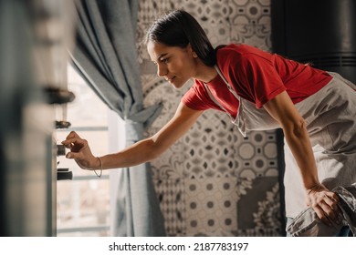 Young Hispanic Brunette Woman Wearing Apron Standing By Oven While Cooking In Kitchen At Home