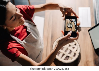 Young Hispanic Brunette Woman Wearing Apron Taking Photo Of Meal While Cooking In Kitchen At Home