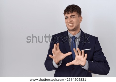 Young hispanic business man wearing suit and tie disgusted expression, displeased and fearful doing disgust face because aversion reaction. with hands raised 