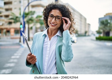 Young hispanic business woman wearing professional look smiling confident at the city holding worker clipboard
