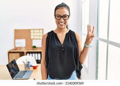 Young Hispanic Business Woman Working At The Office Showing And Pointing Up With Fingers Number Three While Smiling Confident And Happy. 