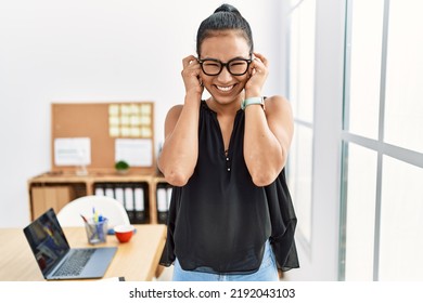 Young hispanic business woman working at the office covering ears with fingers with annoyed expression for the noise of loud music. deaf concept. 