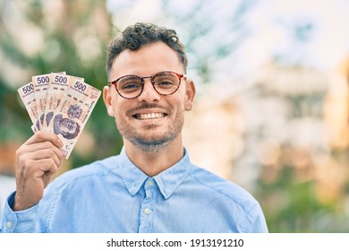 Young hispanic businessman smiling happy holding mexican 500 pesos banknotes at the city.