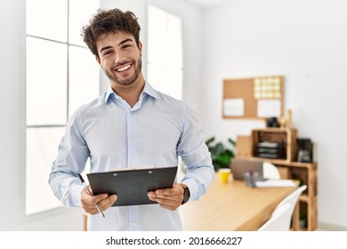 Young hispanic businessman smiling happy holding clipboard at the office.